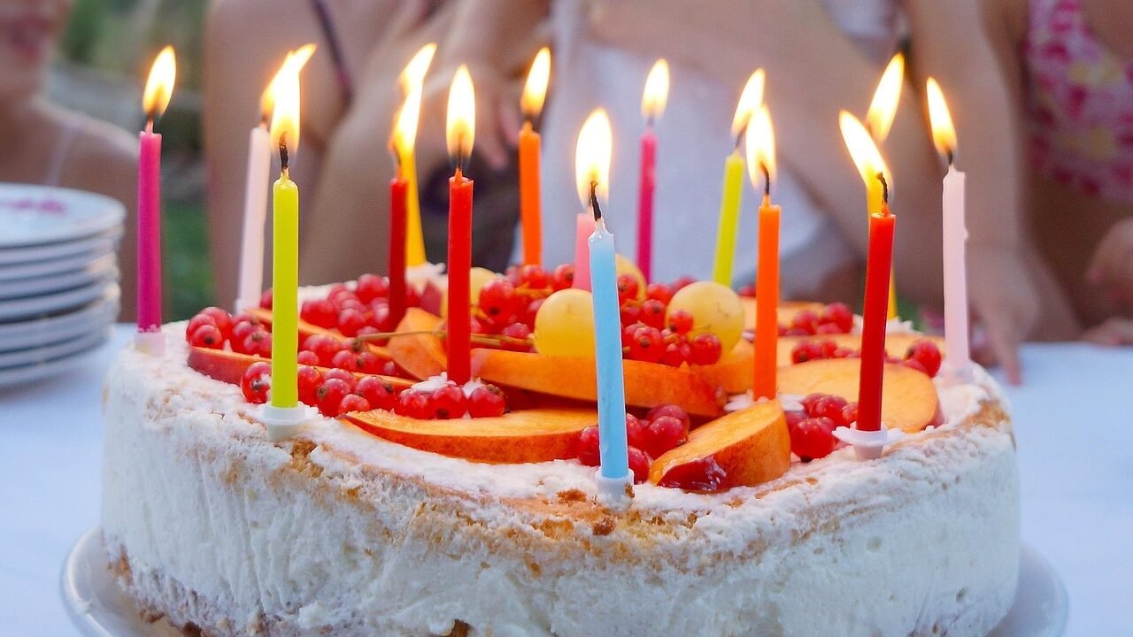 Geburtstagstorte mit Früchten und bunten brennenden Kerzen