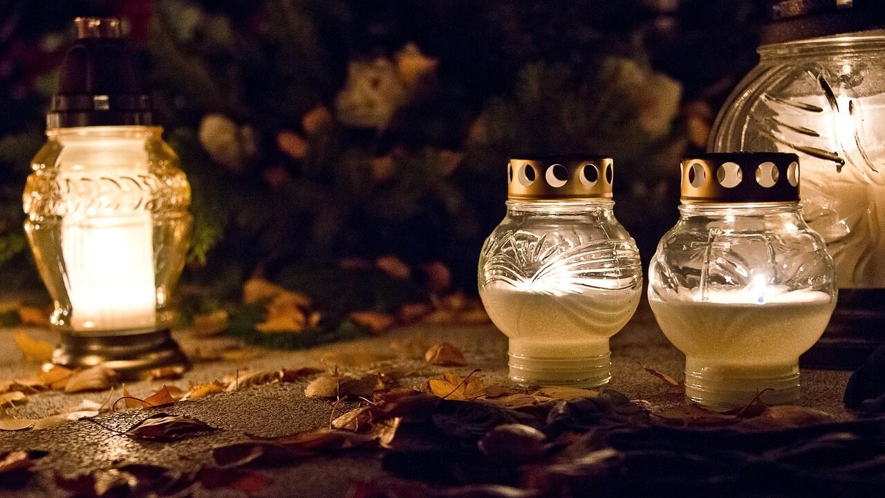 Brennende Grablichter im Herbstlaub auf dem Friedhof