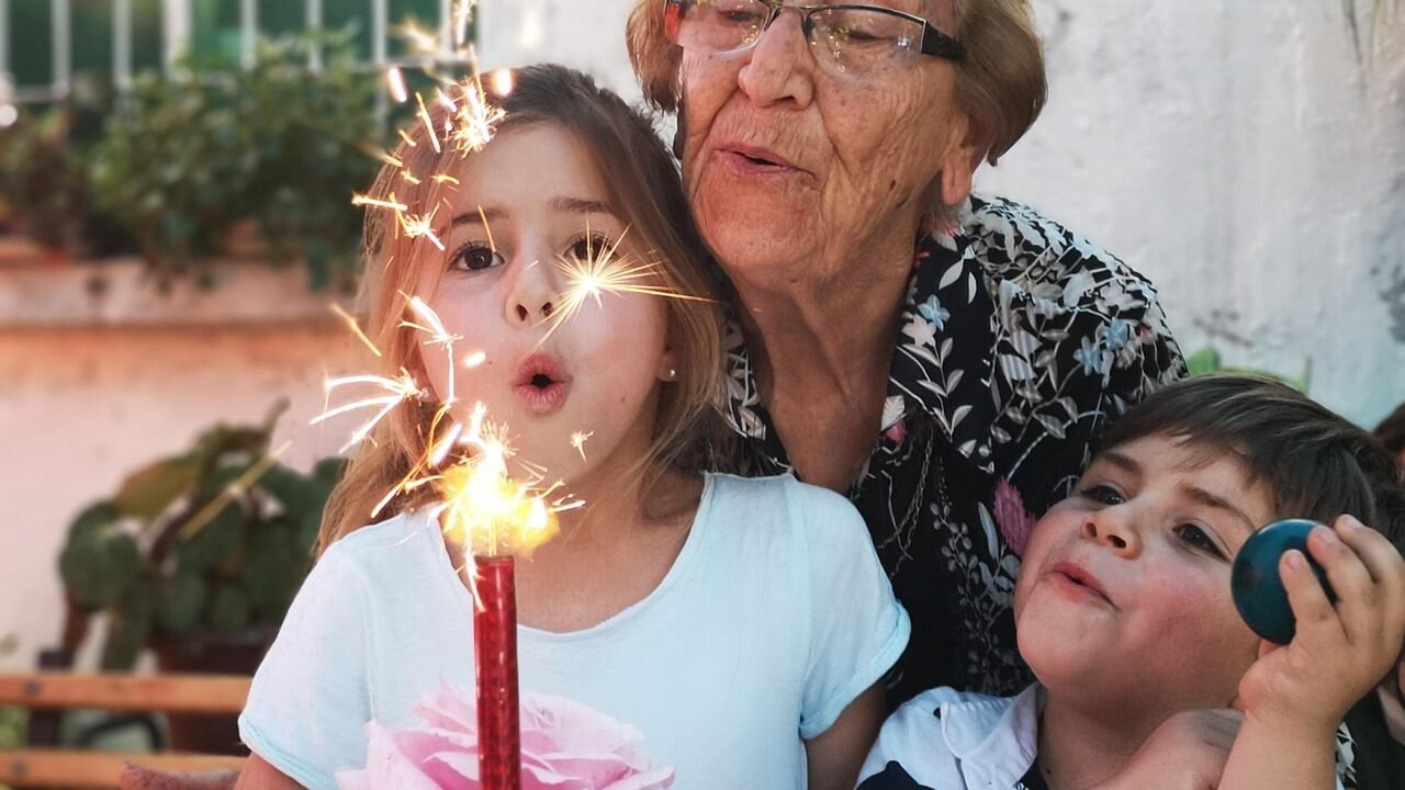 Oma feiert Geburtstag und pustet mit ihren Enkeln die Wunderkerze auf der Torte aus