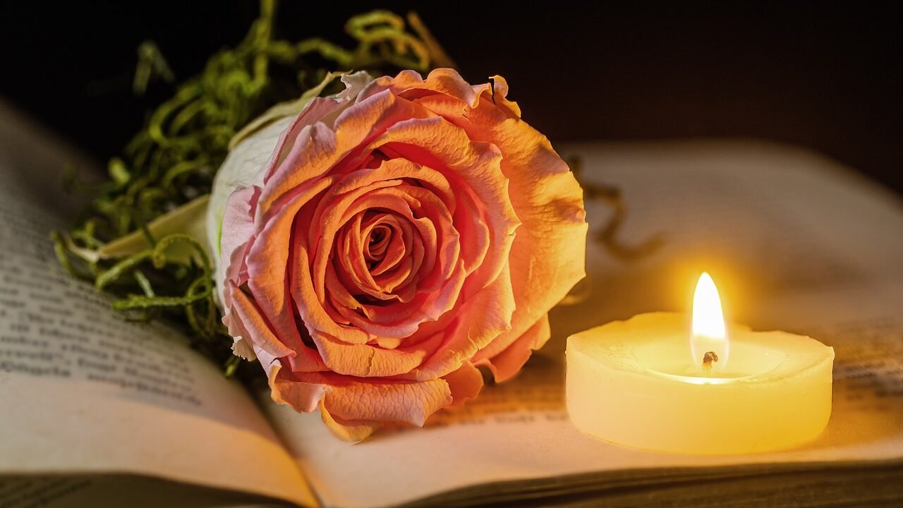 Rose und brennende Kerze neben einem aufgeschlagenen Buch